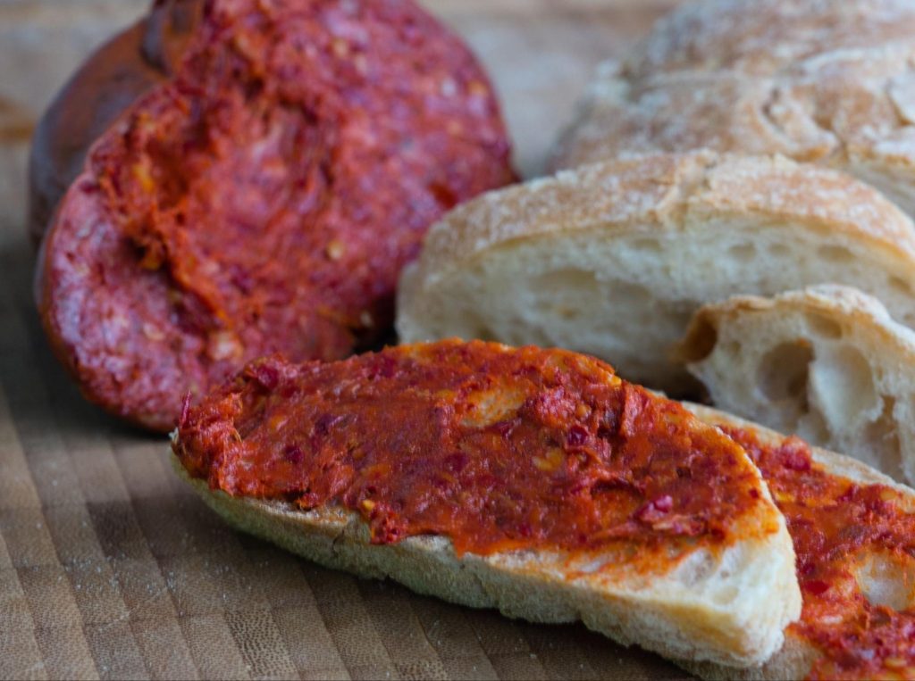 'Nduja with bread, with a piece of 'nduja sausage in background
